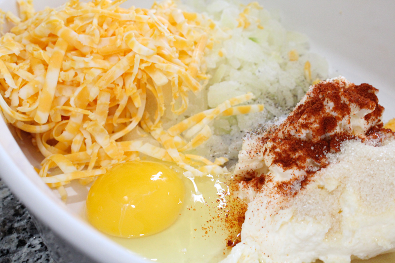 shredded cheese, diced onion, a raw egg, mayonnaise, and seasonings in a white dish