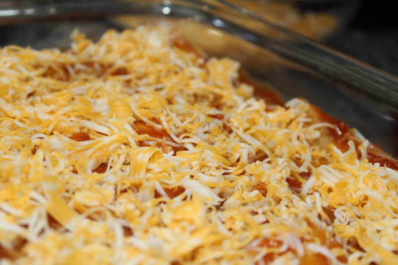 enchiladas from scratch topped with sauce and cheese ready for the oven