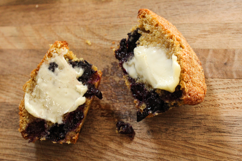 One of the best blueberry muffins cut in half sitting on a cutting board topped with butter