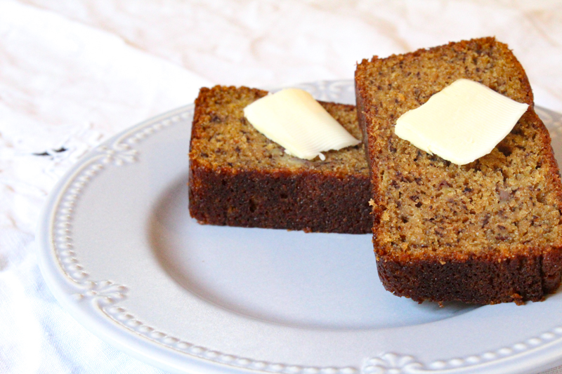 two slices of einkorn banana bread topped with a pad of butter sitting on a light blue plate with a white table cloth
