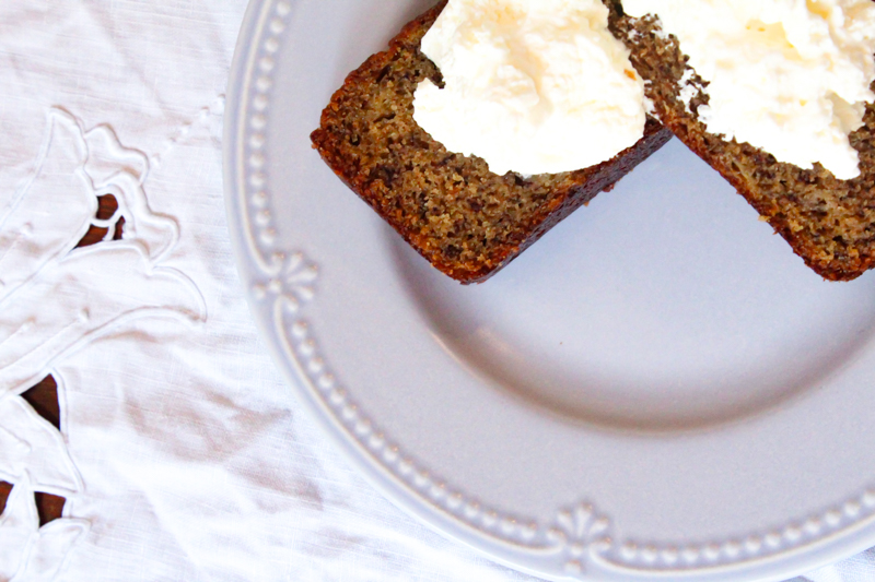 two slices of einkorn banana bread topped with whipped cream on a light blue plate sitting on a white table cloth