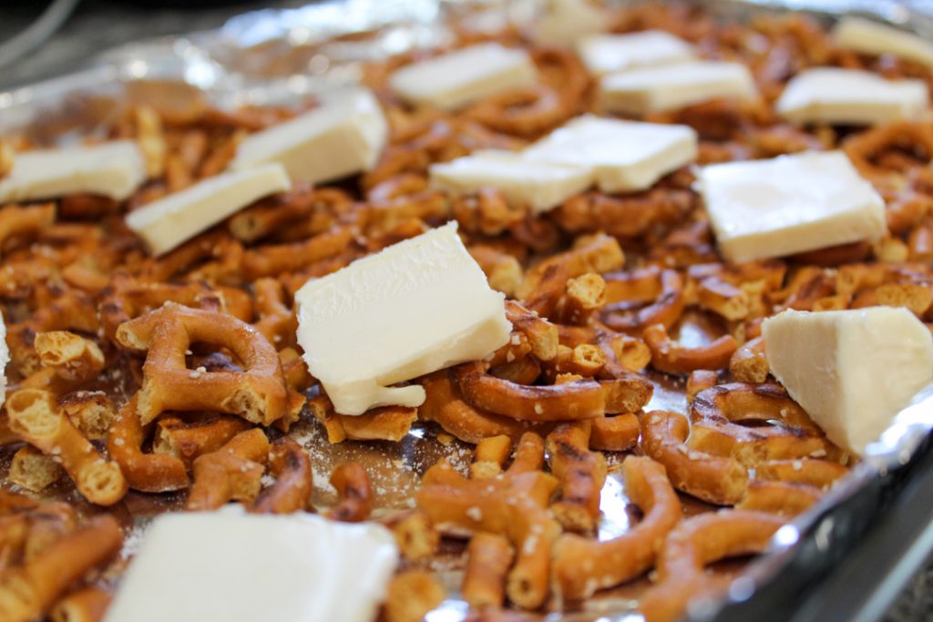broken twisted pretzels on a foiled lined cookie sheet topped with slices of butter. 