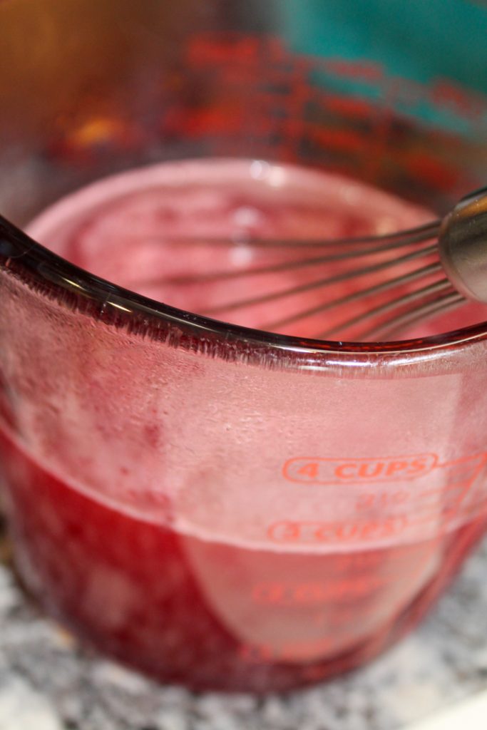 jello and hot water with a whisk sitting in a two cup measuring cup