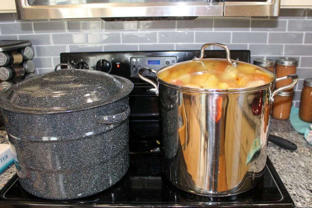 black glass stovetop and oven with a water bath canner on the front left burner and a stockpot full of quartered apples cooking for homemade applesauce using a kitchenaid mixer. 