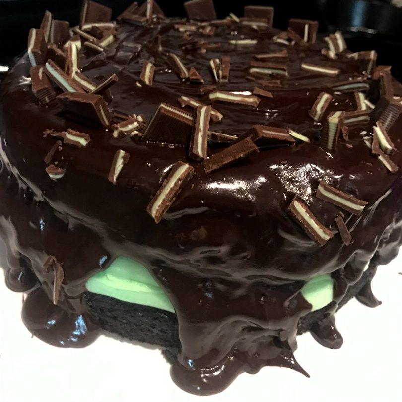 Two layers of chocolate cake with green peppermint buttercream frosting in between them topped with chocolate ganache and andes mint slices on top.
