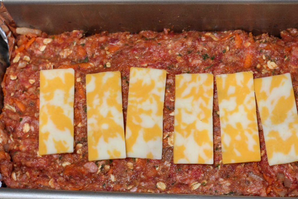 half of the gluten free meatloaf mixture in a meatloaf pan topped with slices of colby jack cheese. 