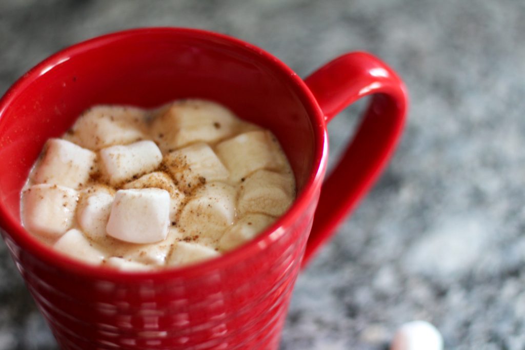 red mug filled with a hot drink topped with mini marshmallows and a dash of nutmeg