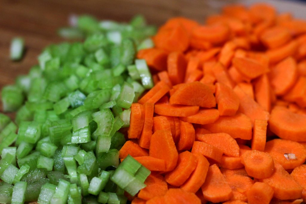 a pile of diced celery on the left and a pile of sliced carrots on the right. They're sitting on a wooden cutting board.