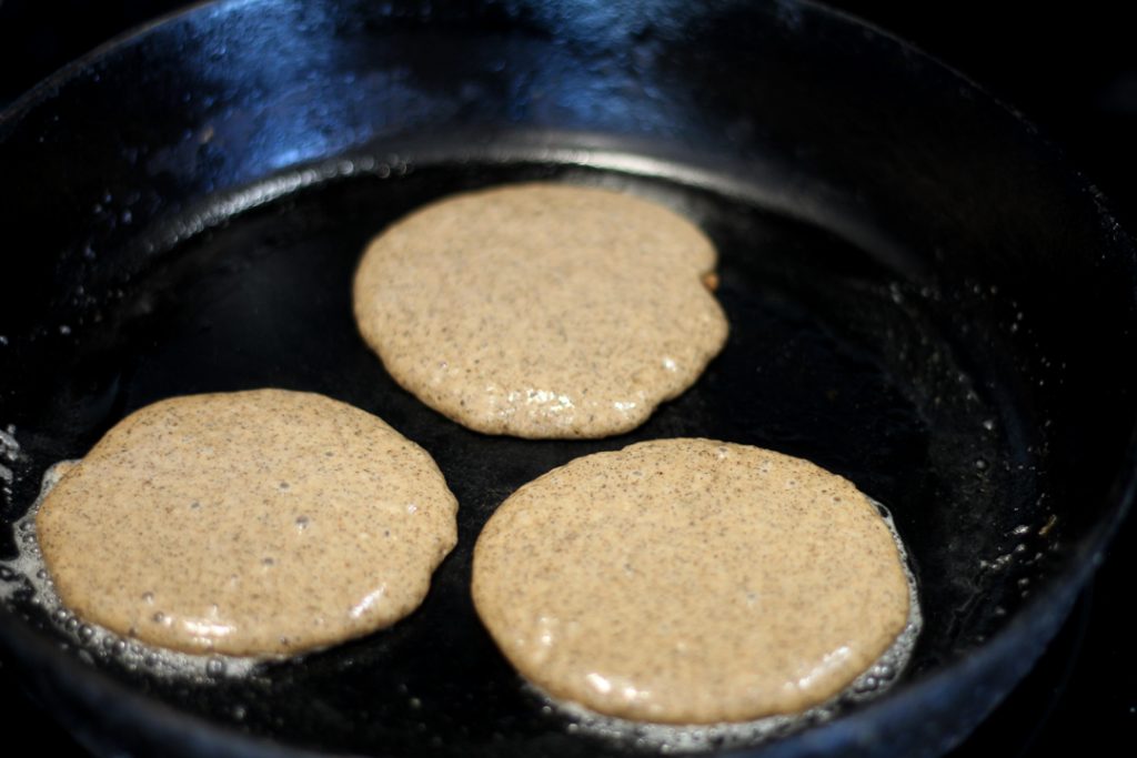 pancake batter cooking in a cast iron skillet. there are three small pancakes cooking