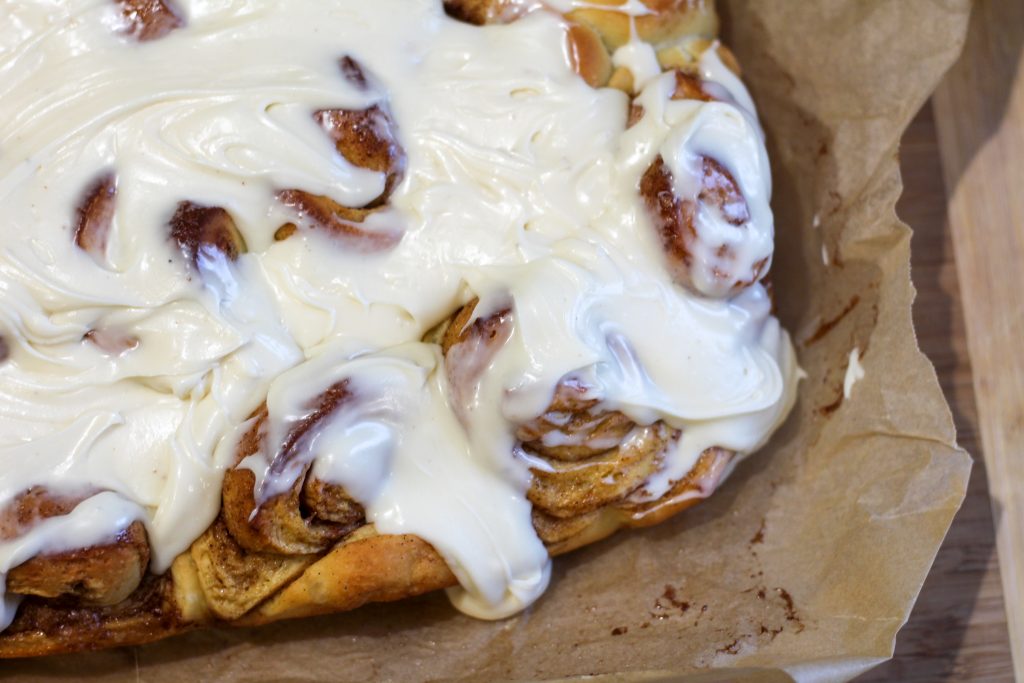 iced honey maple cinnamon rolls sitting on parchment paper on a cutting board