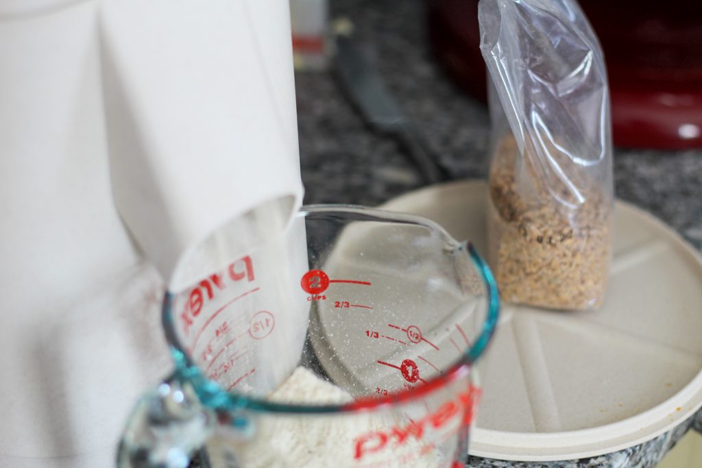 milling einkorn in a mockmill. Grains are in a small bag to the side of the mill and the flour is coming out the spout into a glass measuring cup